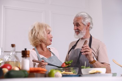 Photo of Elderly couple cooking together at table indoors