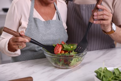 Photo of Elderly couple with spatulas cooking together at white marble table in kitchen, closeup