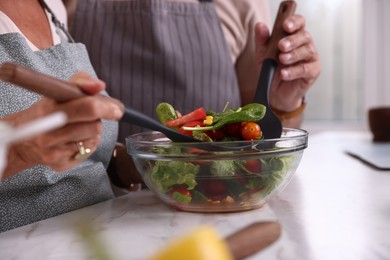 Photo of Elderly couple with spatulas cooking together at white marble table in kitchen, closeup