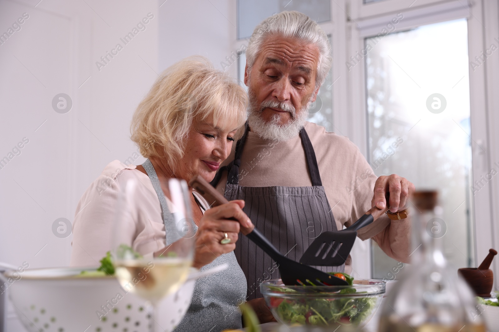 Elderly couple with spatulas cooking together in kitchen Photo of Elderly couple with spatulas cooking together in kitchen