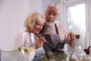 Photo of Elderly couple with spatulas cooking together in kitchen