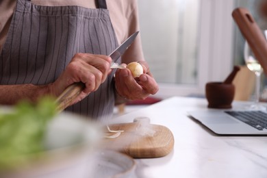 Photo of Elderly man with onion and knife at marble table indoors, closeup