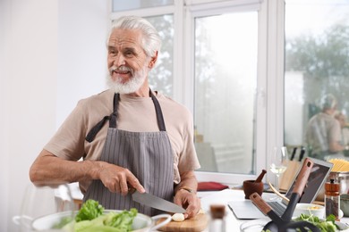 Photo of Smiling elderly man cooking at table near window indoors