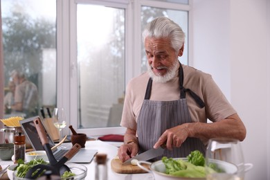 Photo of Elderly man cooking at table near window indoors