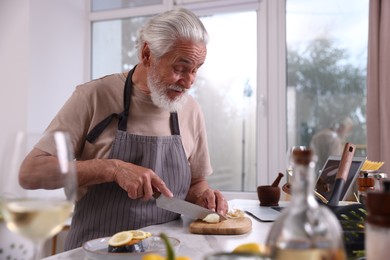 Photo of Elderly man cooking at table near window indoors