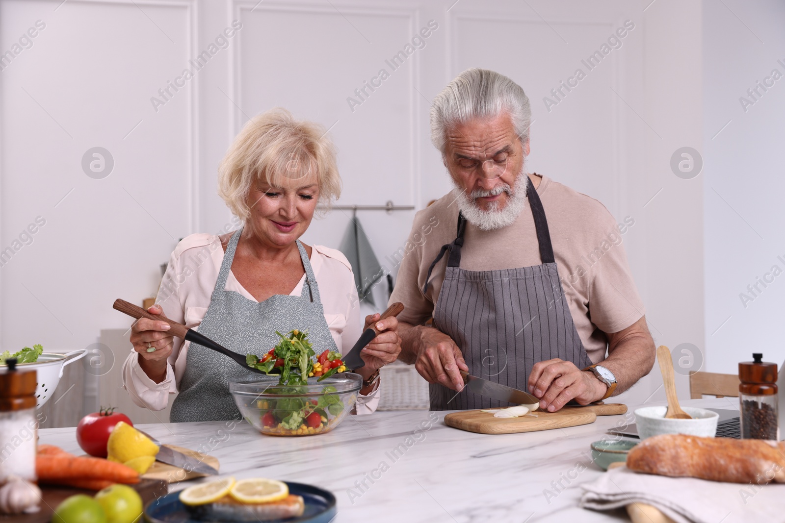 Elderly couple cooking together at marble table in kitchen Photo of Elderly couple cooking together at marble table in kitchen