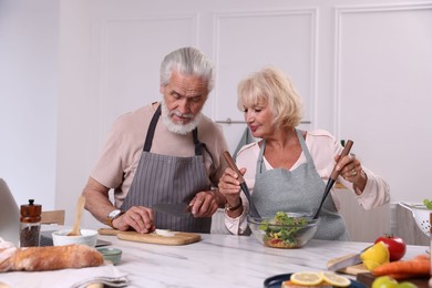 Photo of Elderly couple cooking together at marble table in kitchen