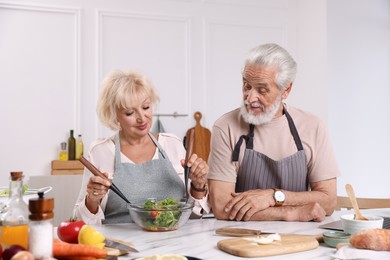 Photo of Elderly couple cooking together at marble table in kitchen