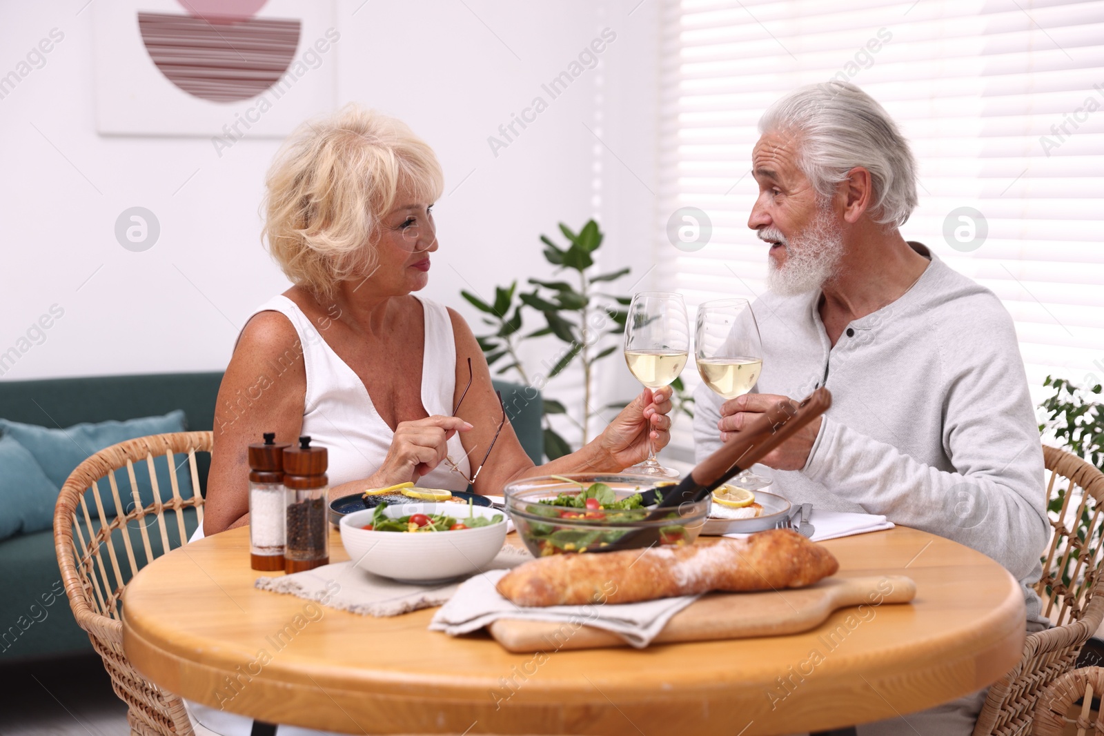 Elderly couple clinking glasses of white wine during dinner at table indoors Photo of Elderly couple clinking glasses of white wine during dinner at table indoors