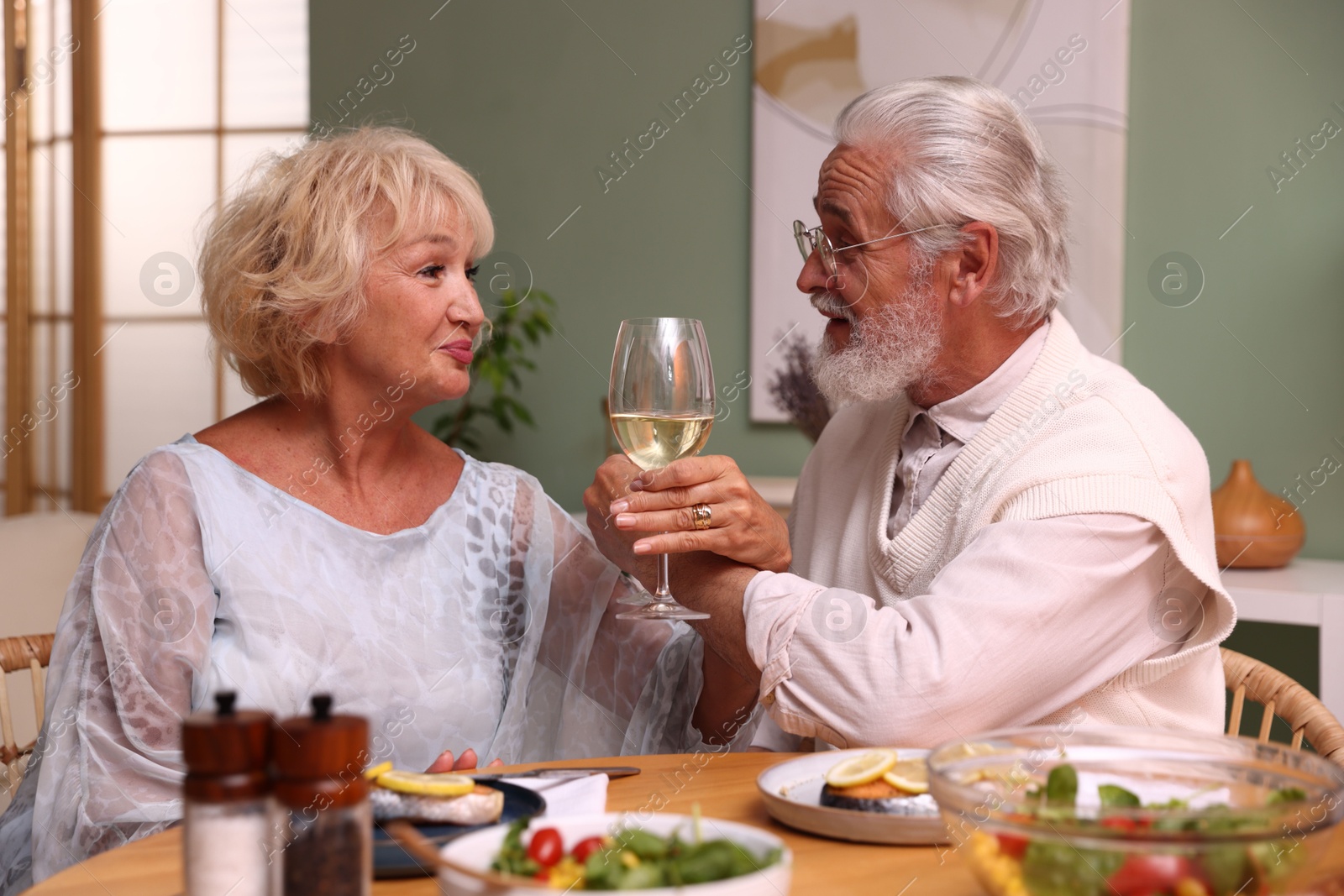 Elderly couple drinking white wine during dinner at table indoors Photo of Elderly couple drinking white wine during dinner at table indoors