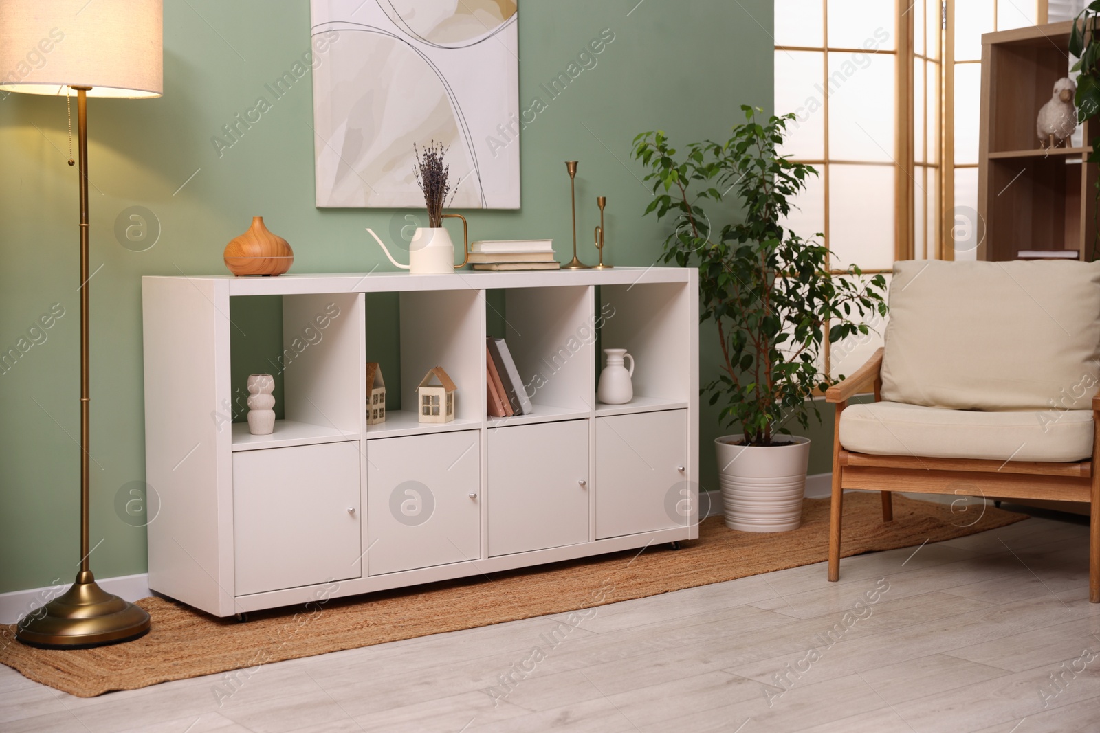 Shelving unit with decorative elements, lamp, houseplant and armchair in stylish room. Interior design Photo of Shelving unit with decorative elements, lamp, houseplant and armchair in stylish room. Interior design