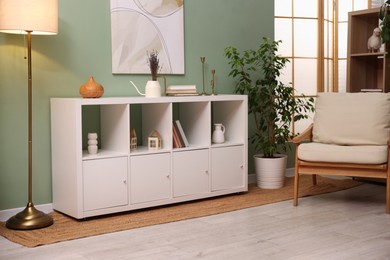 Photo of Shelving unit with decorative elements, lamp, houseplant and armchair in stylish room. Interior design