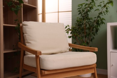 Photo of Stylish armchair near shelving unit and houseplant indoors