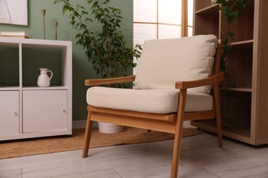 Photo of Stylish armchair near shelving unit and houseplant indoors