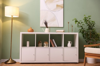 Photo of Shelving unit with decorative elements, lamp and houseplant near green wall indoors