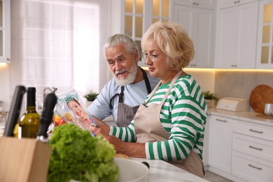 Photo of Elderly couple reading magazine together at table in kitchen