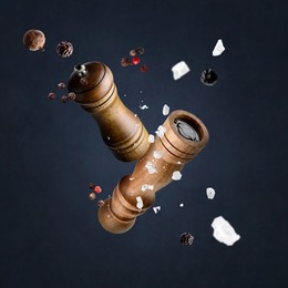 Image of Salt and pepper mills, coarse salt and peppercorns flying against dark background
