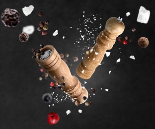 Image of Salt and pepper mills, coarse salt and peppercorns flying against dark background