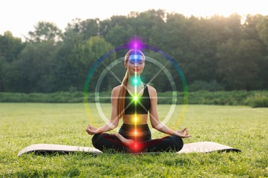 Image of Woman meditating in Lotus pose on green grass. Aura seen as rainbow circle around her. Seven chakras glowing