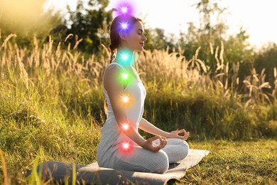Image of Woman meditating in Lotus pose in nature. Seven chakras glowing