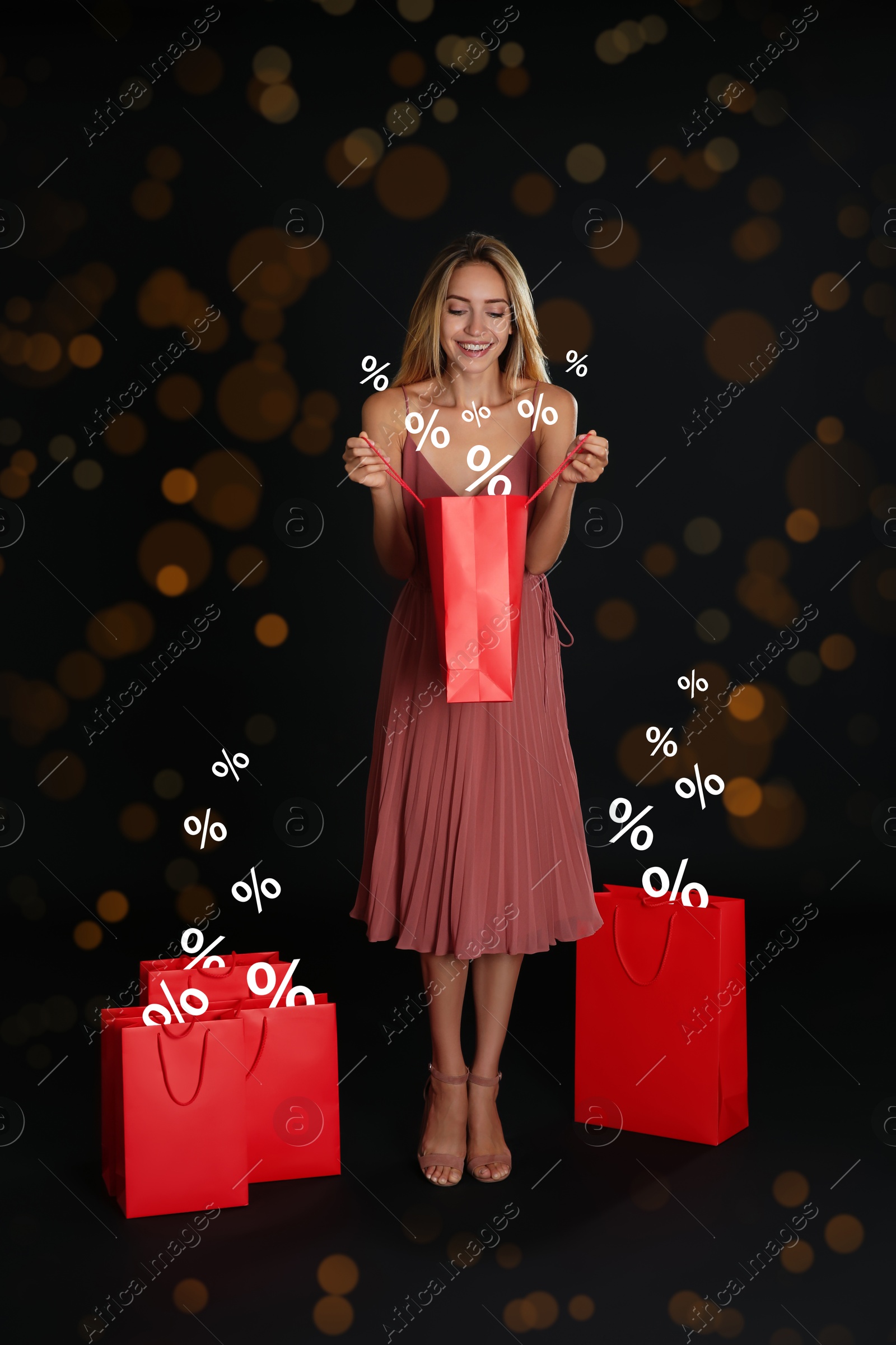 Image of Happy woman with purchases on black background with bokeh lights. Percent signs flying out of shopping bags. Special offer, hot sale
