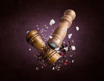 Image of Salt and pepper mills, coarse salt and peppercorns flying against dark purple background