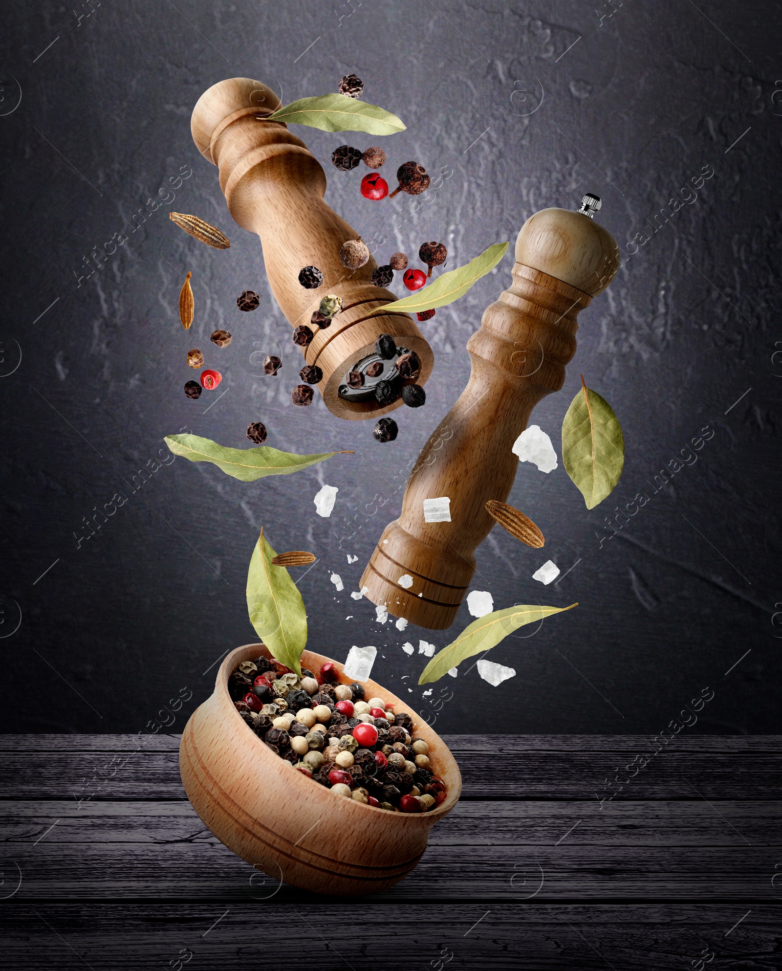 Salt and pepper mills, bowl and spices in air against dark textured background Image of Salt and pepper mills, bowl and spices in air against dark textured background