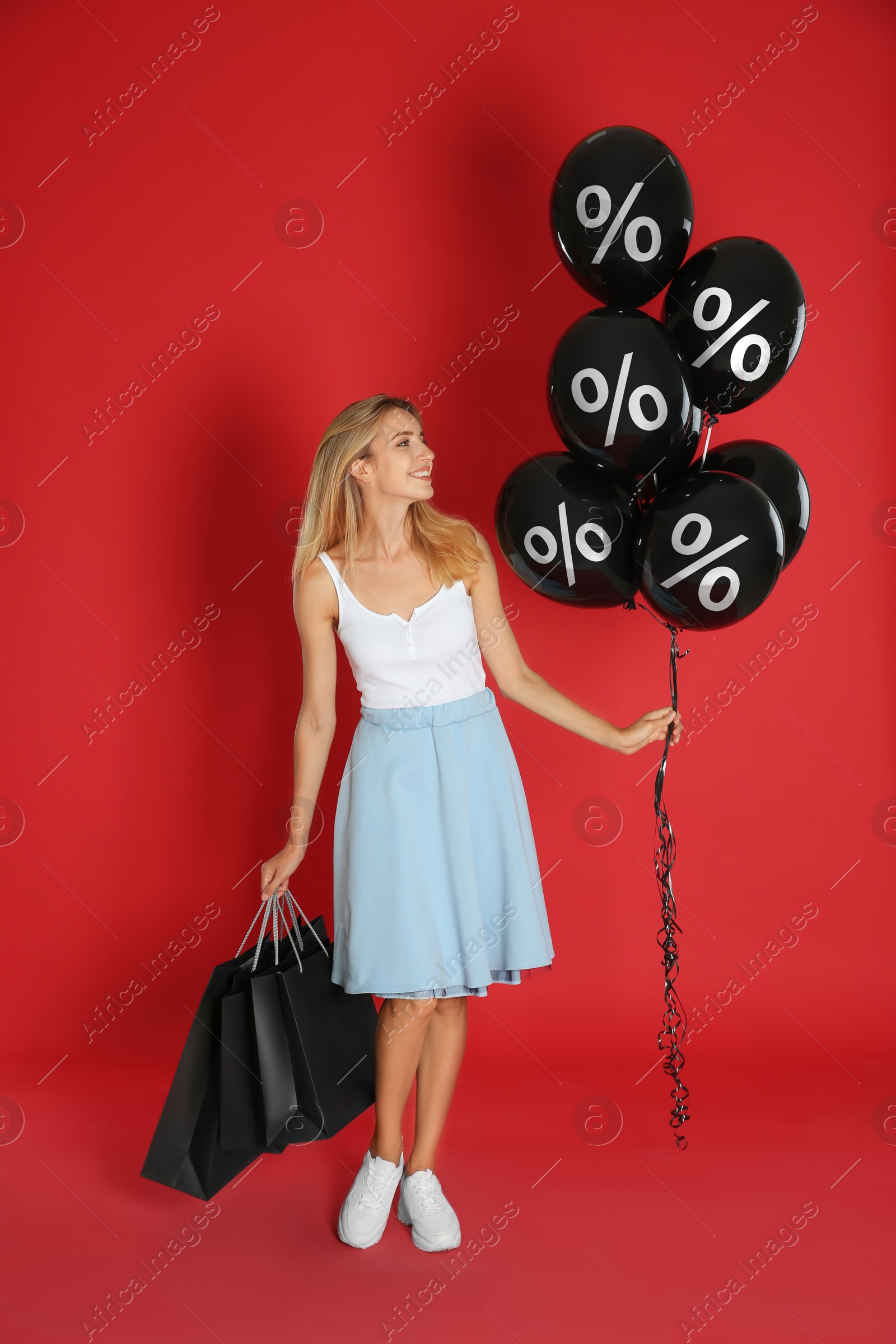 Happy woman with shopping bags holding balloons with percent signs on red background. Special offer, hot sale Image of Happy woman with shopping bags holding balloons with percent signs on red background. Special offer, hot sale