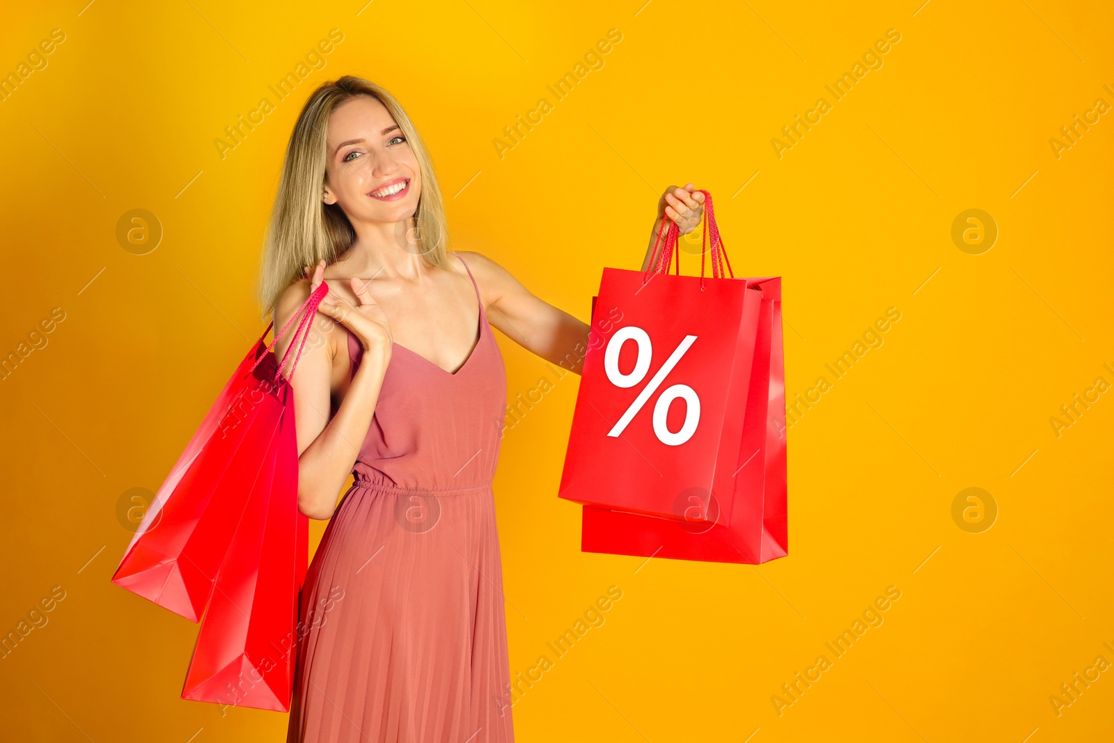Happy woman with purchases on orange background. Red shopping bag with percent sign. Special offer, hot sale Image of Happy woman with purchases on orange background. Red shopping bag with percent sign. Special offer, hot sale