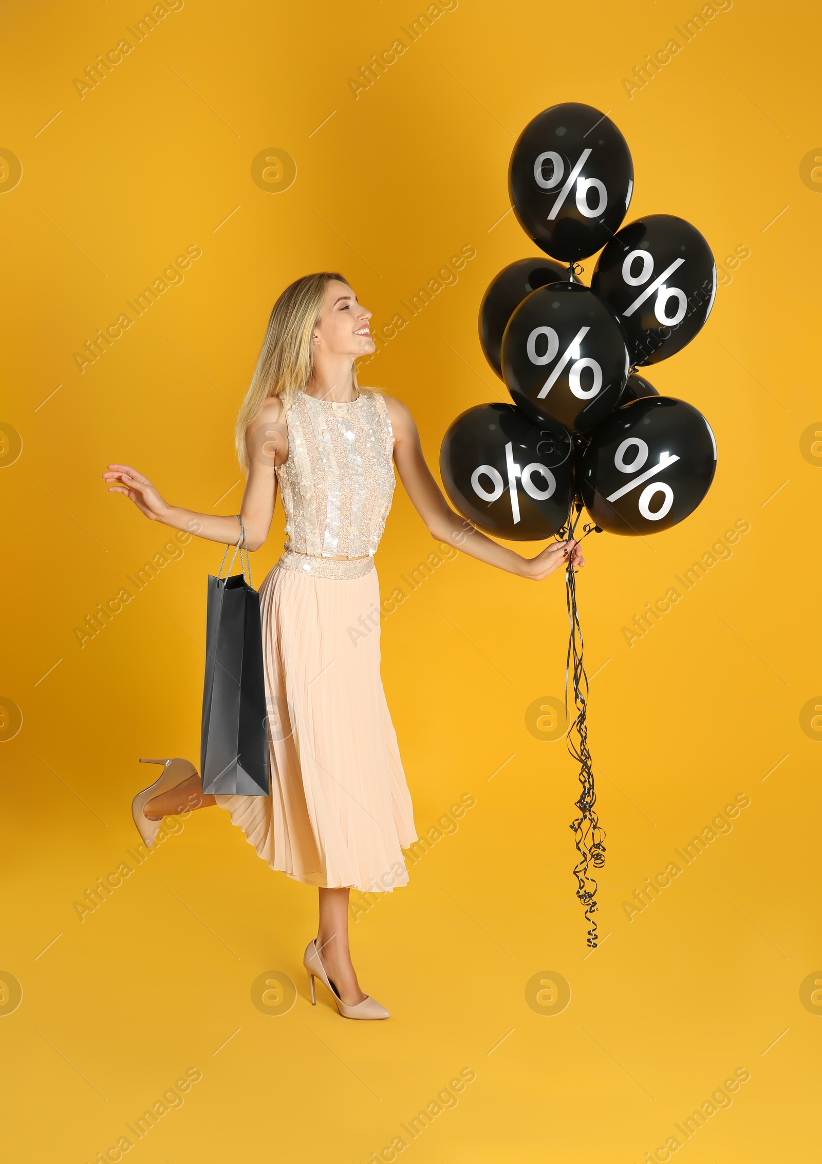 Image of Happy woman with shopping bag holding balloons with percent signs on orange background. Special offer, hot sale