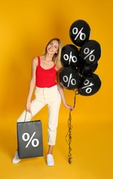 Image of Happy woman with purchase on orange background. Shopping bag and balloons with percent signs. Special offer, hot sale