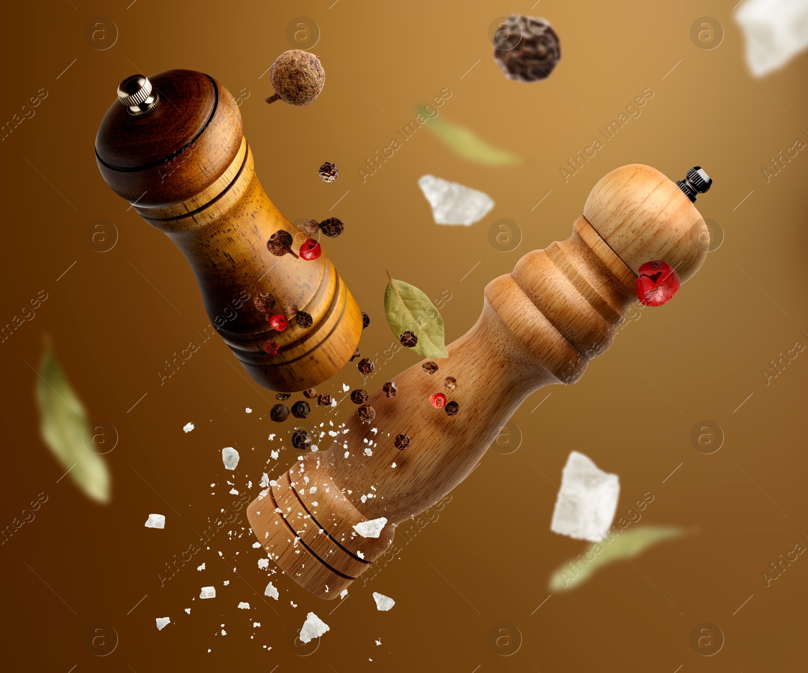 Image of Salt and pepper mills, bay leaves, coarse salt and peppercorns flying against brown gradient background
