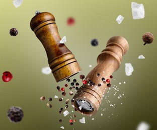 Image of Salt and pepper mills, coarse salt and peppercorns flying against olive gradient background