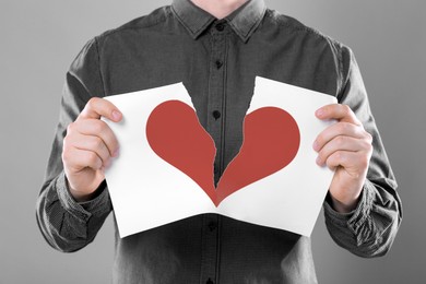 Image of Betrayal. Man tearing sheet of paper with red heart into halves on grey background, closeup