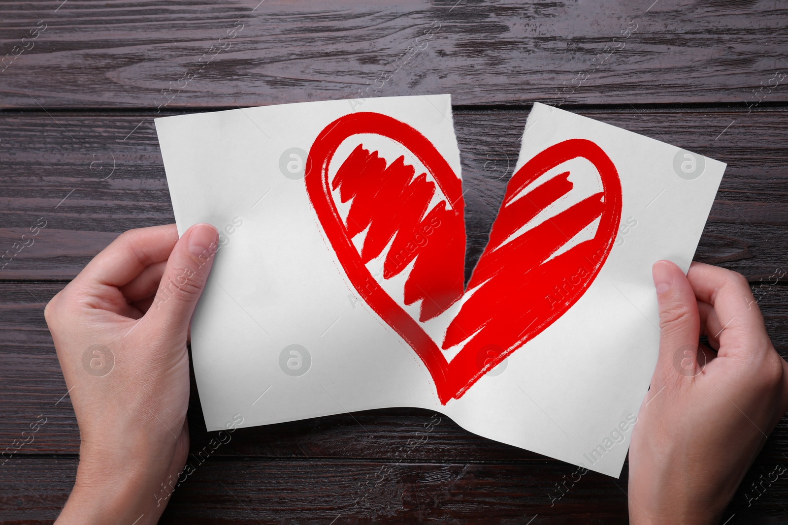 Betrayal. Woman tearing sheet of paper with red heart into halves on wooden background, closeup Image of Betrayal. Woman tearing sheet of paper with red heart into halves on wooden background, closeup