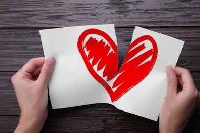 Image of Betrayal. Woman tearing sheet of paper with red heart into halves on wooden background, closeup