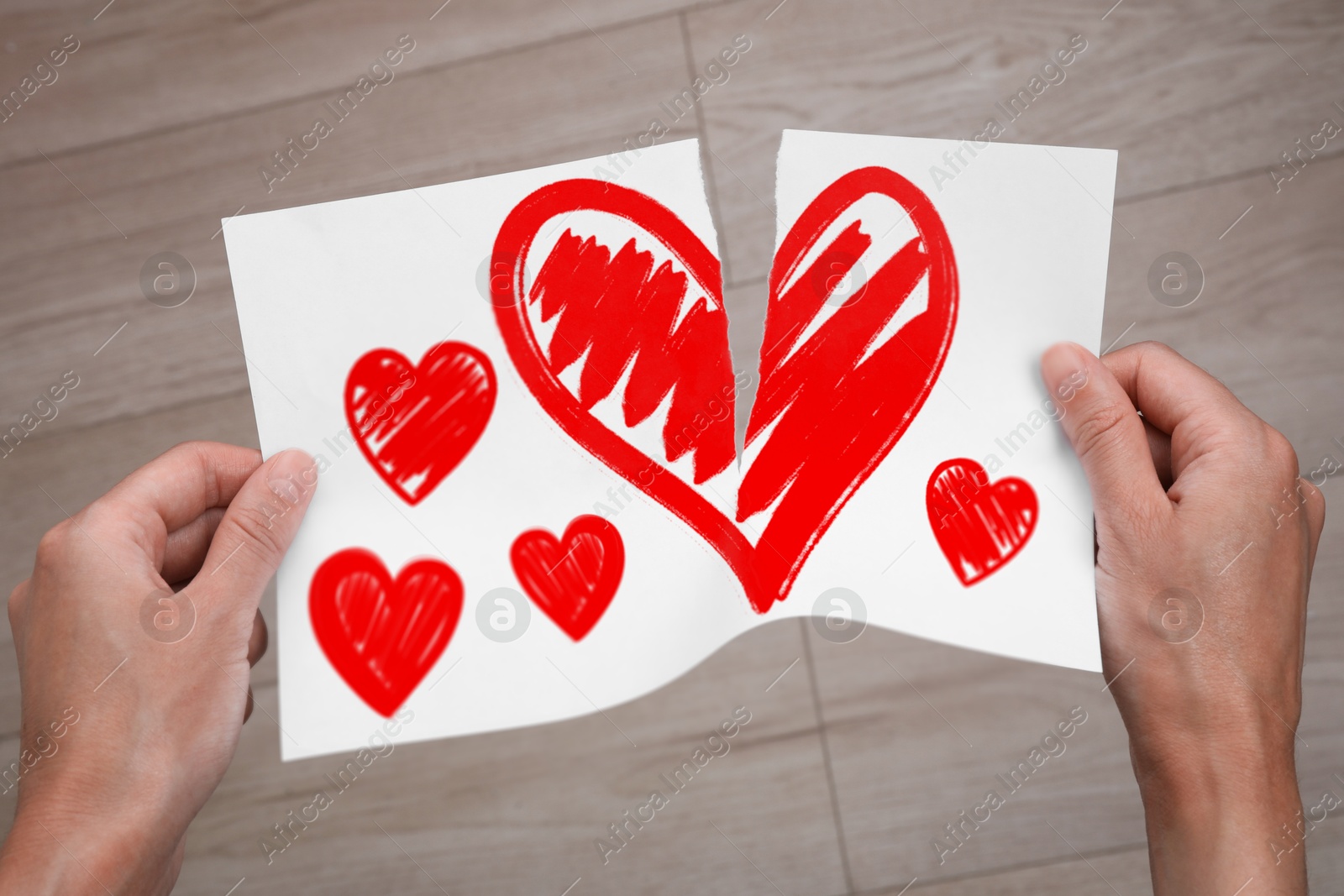 Betrayal. Man tearing sheet of paper with red hearts indoors, closeup Image of Betrayal. Man tearing sheet of paper with red hearts indoors, closeup