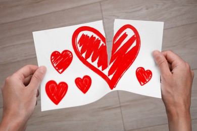 Image of Betrayal. Man tearing sheet of paper with red hearts indoors, closeup