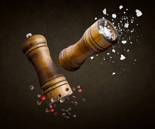 Image of Salt and pepper mills, coarse salt and peppercorns flying against dark brown background
