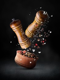 Image of Salt and pepper mills, bowl, coarse salt and peppercorns in air against black background