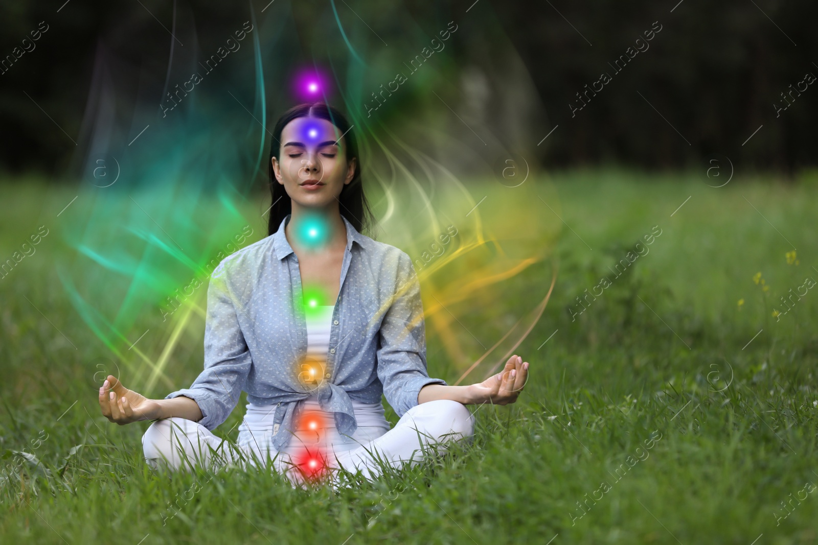 Woman meditating in Lotus pose on green grass. Aura seen as rainbow waves around her. Seven chakras glowing Image of Woman meditating in Lotus pose on green grass. Aura seen as rainbow waves around her. Seven chakras glowing