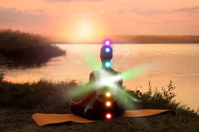 Image of Woman meditating in Lotus pose near river at sunrise . Seven chakras glowing