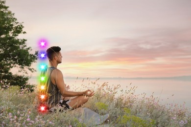 Image of Man meditating in Lotus pose near river. Seven chakras glowing