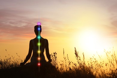 Image of Woman meditating in Lotus pose in nature at sunrise. Seven chakras glowing
