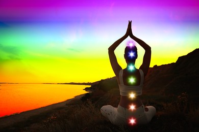 Image of Woman meditating in Lotus pose near sea, toned in rainbow colors. Seven chakras glowing