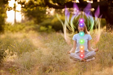 Image of Woman meditating in Lotus pose in nature. Aura seen as rainbow waves around her. Seven chakras glowing