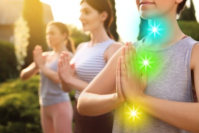 Image of Women practicing yoga and meditation outdoors on sunny day, closeup. Colorful chakras glowing