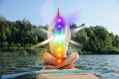 Image of Man meditating in Lotus pose on SUP board. Seven chakras glowing
