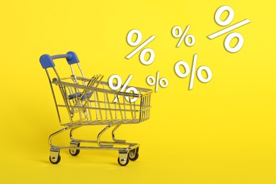 Image of Hot sale, special offer. Percent signs flying out of shopping cart against yellow background