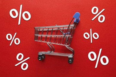 Image of Hot sale, special offer. Percent signs and shopping cart on red background, top view